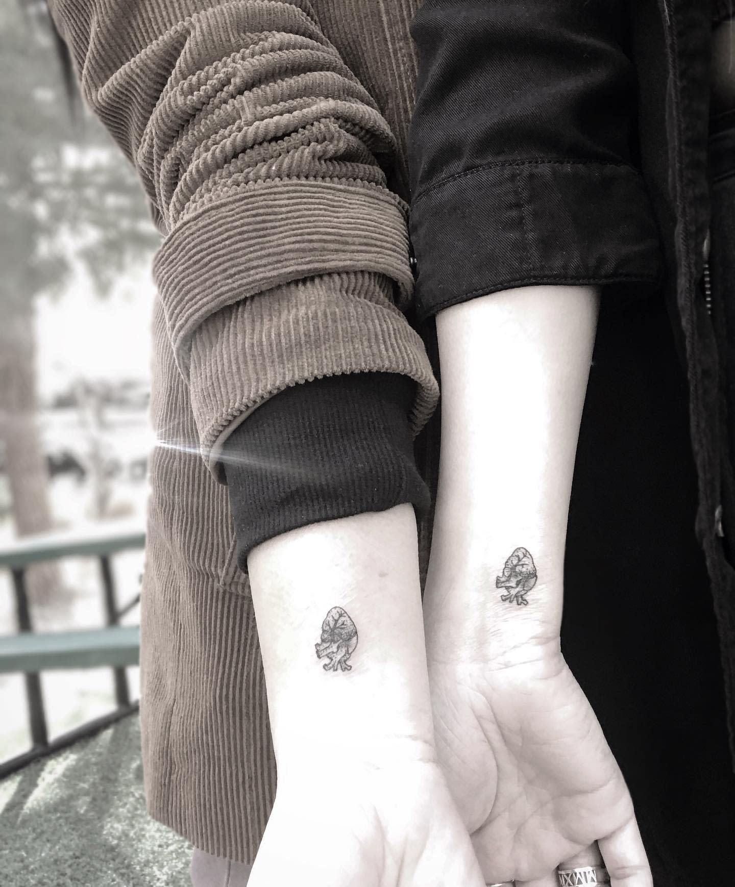 Two individuals displaying small heart matching tattoos on their inner wrists
